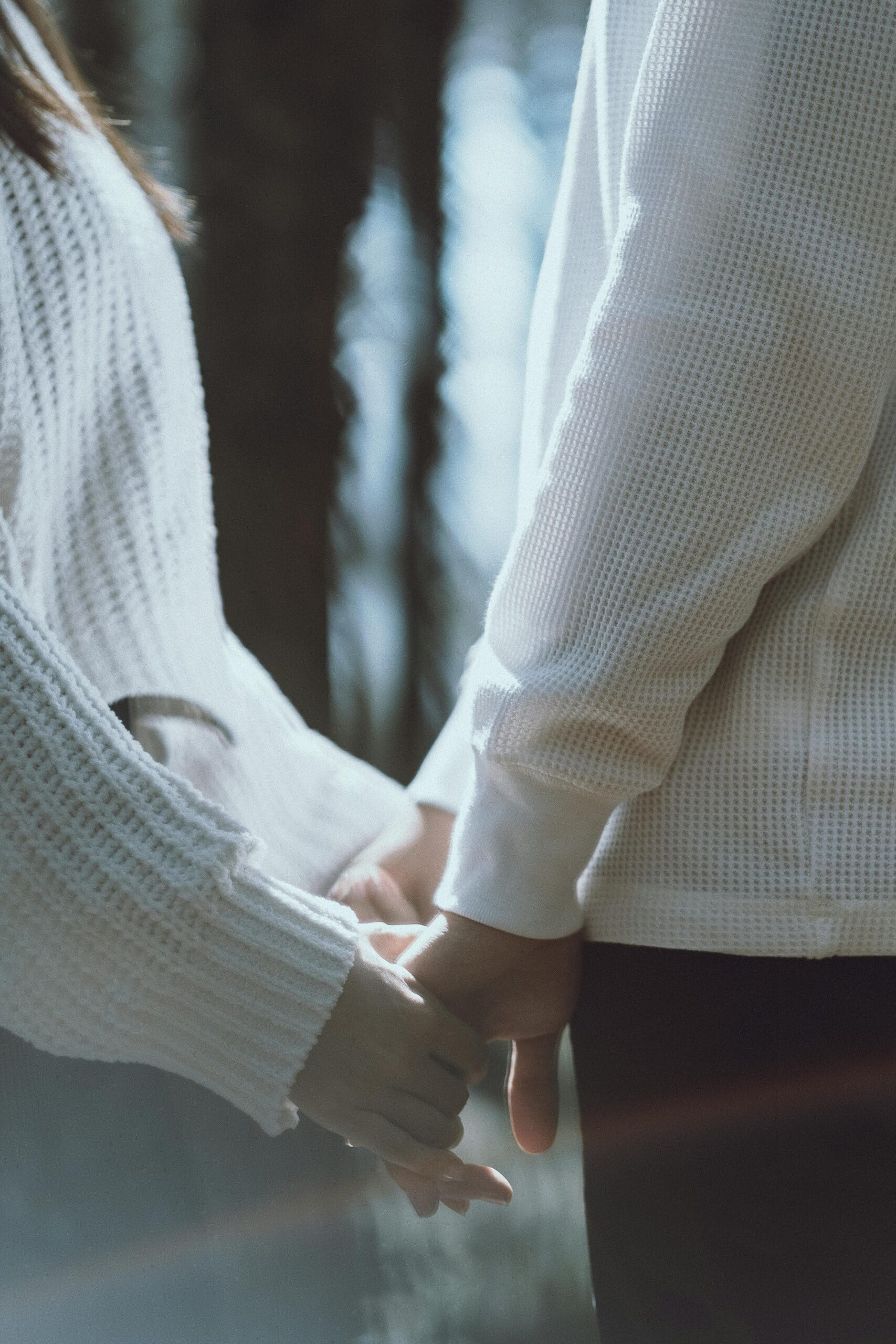 Two people in white knit sweaters gently hold hands in a softly lit close-up. Could codependency be making it hard to feel balanced and secure in relationships? Relational trauma therapy in Palm Beach, FL, can help you reconnect.