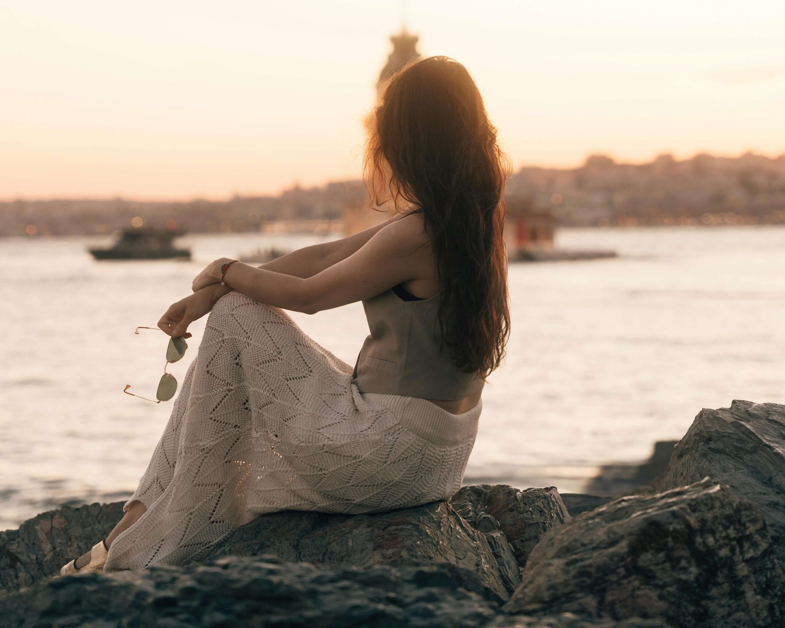 A woman sits alone on coastal rocks at sunset. Are unresolved trauma patterns causing you to withdraw or feel disconnected in your relationships? Relational trauma therapy in Palm Beach, FL, offers compassionate support to help you reconnect and heal.
