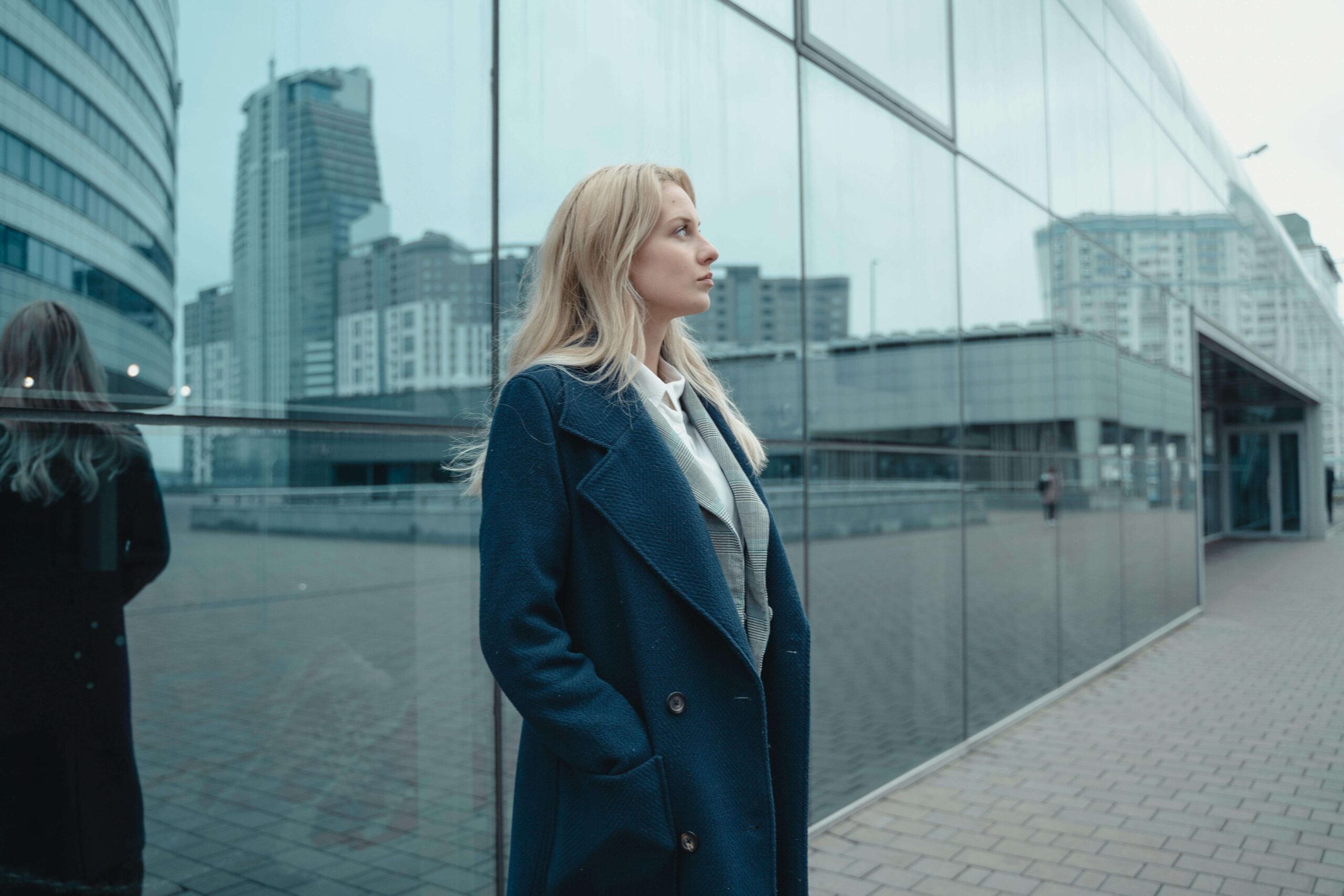 A woman in a navy coat stands before a glass building reflecting the city. Could unresolved trauma be the hidden force preventing high achievers like you from feeling truly fulfilled? Relational trauma therapy in Palm Beach, FL helps you identify and break through those invisible barriers.