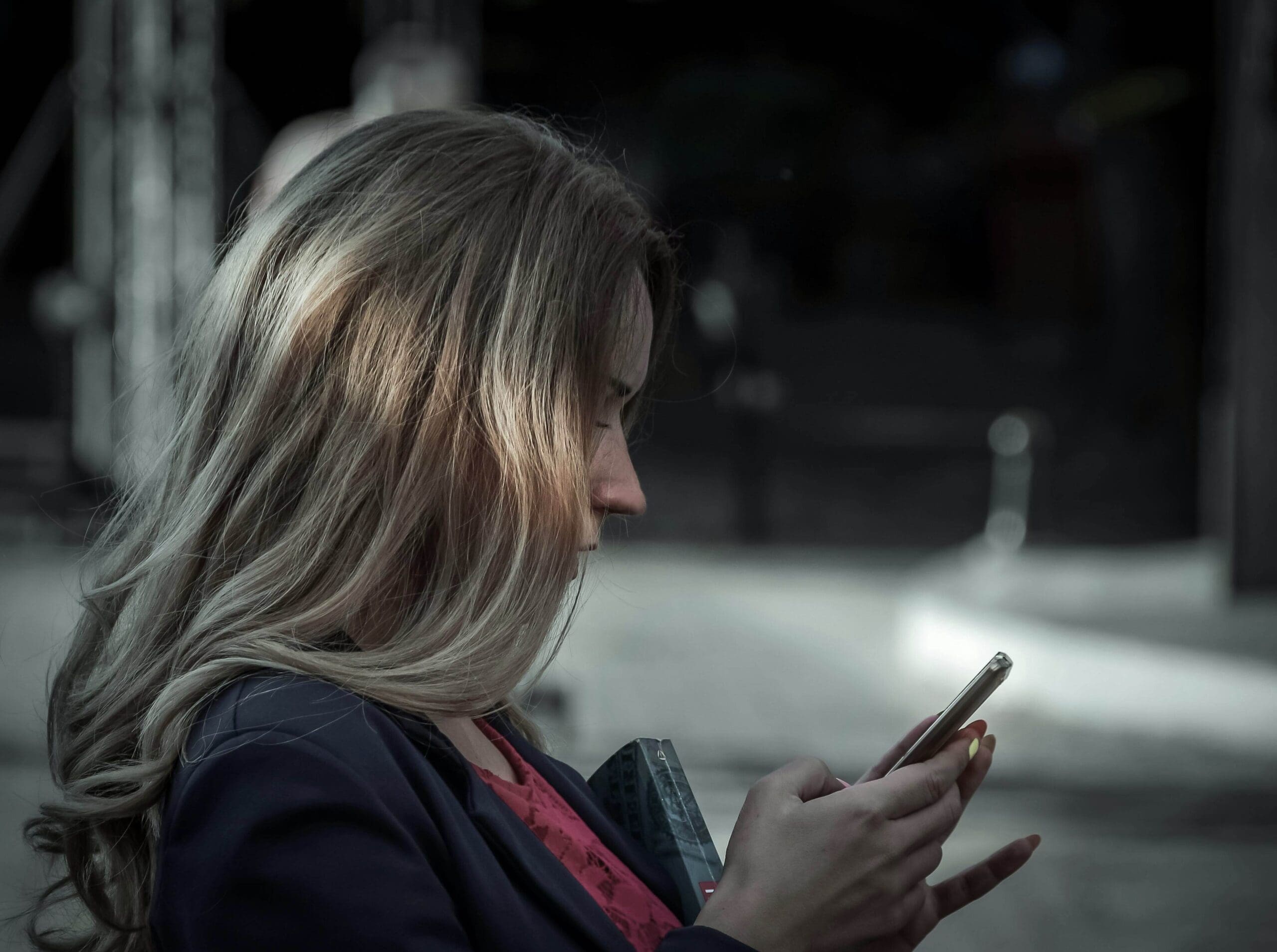 A woman looks down at her phone, appearing reflective. Could trauma influence the need to stay constantly available or agreeable to others? A relational trauma therapist in Palm Beach, FL, can help process these underlying emotional patterns.