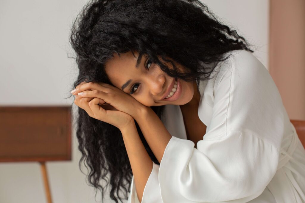 Woman smiling | online relational trauma therapist palm beach | complex ptsd online therapist palm beach, fl | relational trauma therapy | Palm Beach, Florida | Wellington | Boynton Beach | The Island | The Colony Hotel A woman smiles warmly, resting her chin gently on her clasped hands. Can therapy help you feel like yourself again? Online relational trauma therapy in Palm Beach, FL offers a space to reconnect with your own sense of ease.