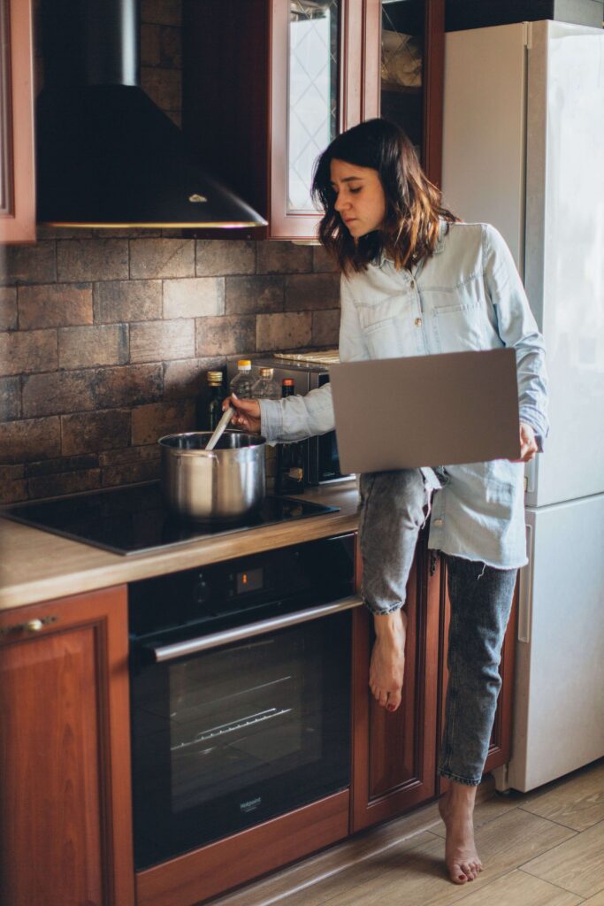 Woman cooking | relationship burnout palm beach | trauma therapy for high achievers palm beach | relational trauma therapy | Palm Beach, Florida | Jupiter | Palm Beach Gardens | Wall Street South | Whitehall A woman stirs a pot on the stove while balancing a laptop in the kitchen. Why does relationship burnout so often come from doing it all at once? A relational trauma therapist in Palm Beach, FL can help you untangle these competing demands.