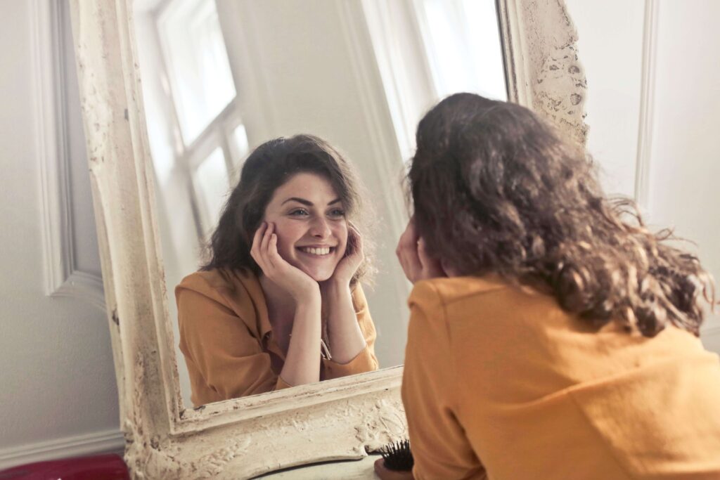 Woman smiling | how to find a therapist palm beach | complex ptsd online therapist palm beach, fl | relational trauma therapy | Palm Beach, Florida | Wellington | Boynton Beach | The Island | The Colony Hotel A woman smiles warmly at her own reflection in a vintage mirror. What does it feel like to find the right therapist? An online relational trauma therapist in Palm Beach, FL helps you rebuild trust in yourself and others.