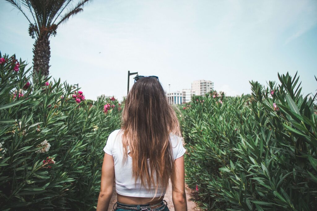 A woman with long hair walks away through tall green foliage, her back to the camera. Does closeness with others sometimes trigger an urge to pull away or shut down? An online relational trauma therapist in Palm Beach, FL can help you work through this response.