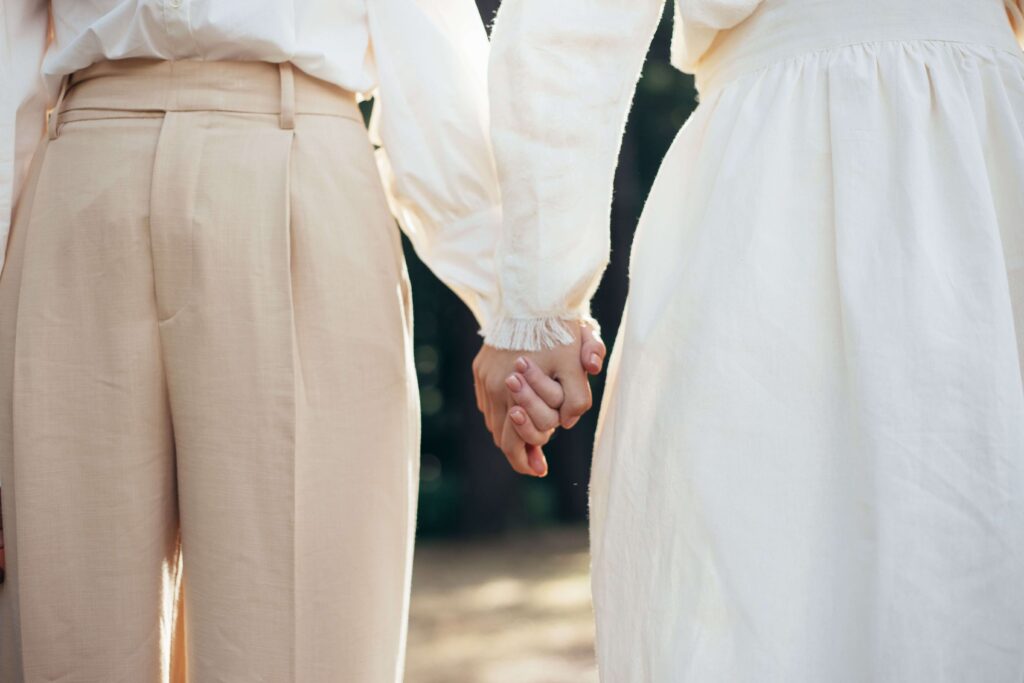 A couple holds hands tenderly while standing close together outdoors. Does avoidant attachment make even small moments of closeness feel overwhelming? Online relational trauma therapy in Palm Beach, FL can help you understand these patterns.
