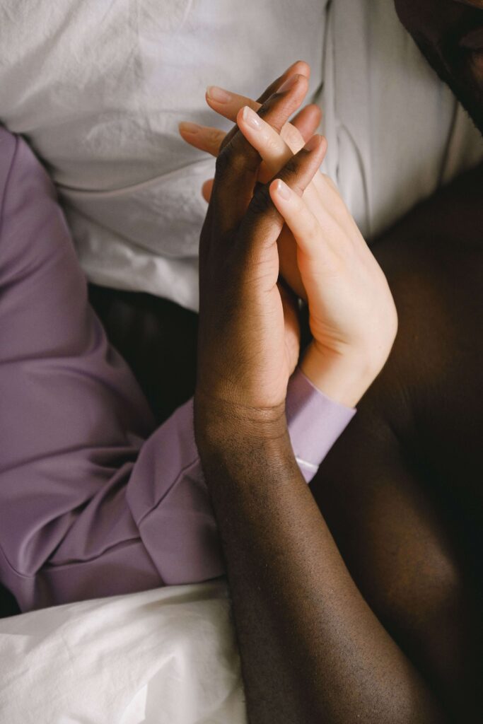 Holding hands | anxious attachment therapy palm beach | complex ptsd online therapist palm beach, fl | relational trauma therapy | Palm Beach, Florida | Wellington | Boynton Beach | The Island | The Colony Hotel A couple holds hands tenderly, their fingers intertwined against soft bedding. Does anxious attachment make it hard to simply relax and trust in your relationship? Online relational trauma therapy in Palm Beach, FL can help you build a felt sense of safety.