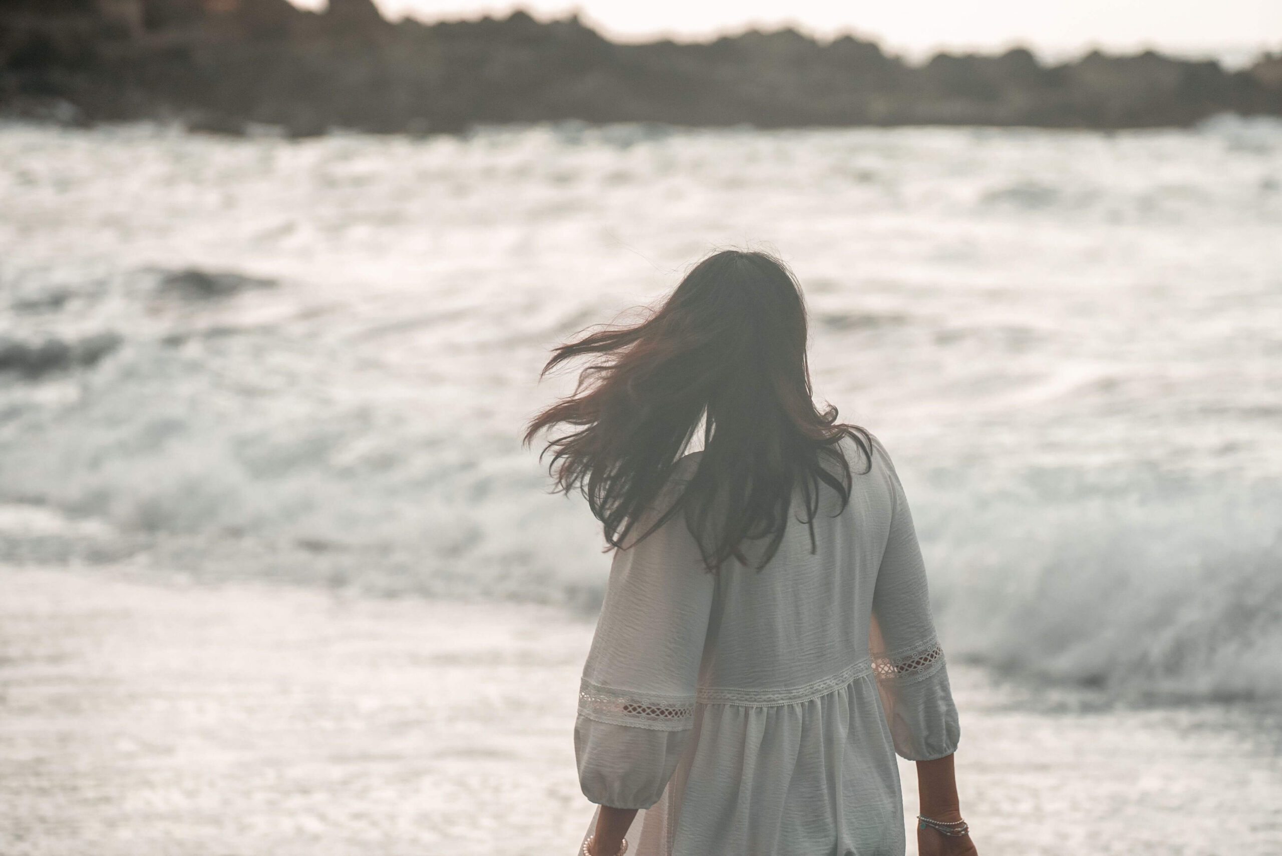 A woman stands alone at the shore, her hair blowing as she faces the waves. Could feeling emotionally disconnected be your mind's way of coping with past pain? An online relational trauma therapist in Palm Beach, FL can help you reconnect with your emotions.